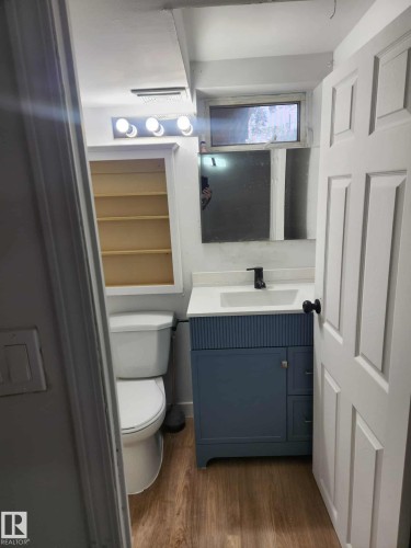 Bathroom featuring a blue vanity with fluted detailing, a rectangular sink with a matte black faucet, and wood-finish flooring - 11308 94 Street, Edmonton, AB 