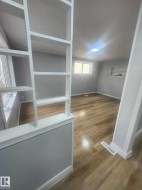 Open-concept interior featuring wood-finish flooring, light gray walls, built-in shelving, and a recessed ceiling light fixture - 