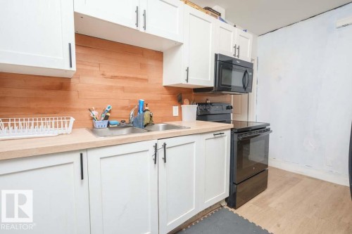 Kitchen featuring white shaker-style cabinetry, wood-finish backsplash, and light-toned countertops - 11308 94 Street, Edmonton, AB 