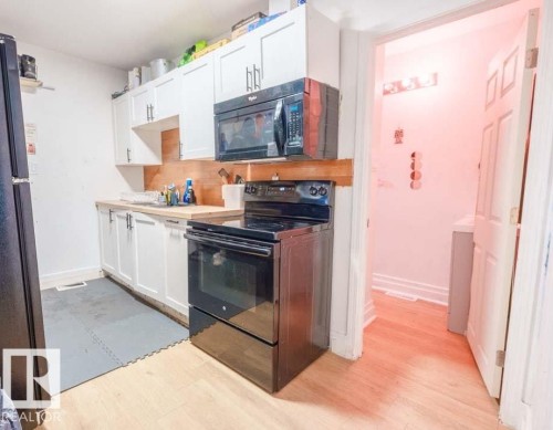 Compact kitchen featuring white cabinetry, light wood-finish countertops, and black appliances including a refrigerator, range, and microwave - 11308 94 Street, Edmonton, AB 