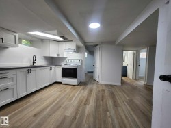 Kitchen space featuring wood-finish flooring, white cabinetry with matte black hardware, a black kitchen faucet, and dark countertops - 