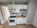 Efficient kitchen space featuring white shaker cabinetry, wood-finish countertops, stainless steel sink with a matte black faucet, a white electric range, and an over-the-range microwave - 11308 94 Street, Edmonton, AB 