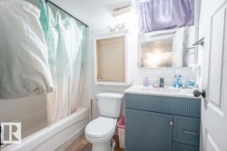 Bathroom featuring a white bathtub with shower, white toilet, and a vanity with a white countertop and blue cabinetry - 