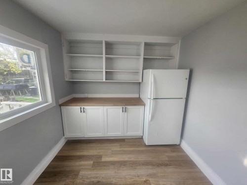 Compact kitchen area featuring white cabinetry with dark hardware, wood-finish countertops, open shelving, and a prominent window - 11308 94 Street, Edmonton, AB 