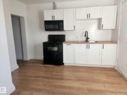 Kitchen area featuring wood-finish flooring, white cabinetry with black hardware, an over-the-range microwave, and a black electric range - 