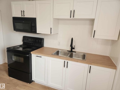 Kitchen featuring white shaker cabinetry with matte black hardware, wood-finish countertops, and a dual stainless-steel sink with a matte black faucet - 11308 94 Street, Edmonton, AB 
