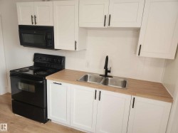 Kitchen featuring white shaker cabinetry with matte black hardware, wood-finish countertops, and a dual stainless-steel sink with a matte black faucet - 