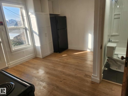 Open-concept room featuring wood-finish flooring, a double-door storage cabinet, and a black refrigerator - 11308 94 Street, Edmonton, AB 