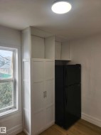 Kitchen area featuring a black refrigerator, tall white pantry cabinetry with silver hardware, upper open shelving, and wood-finish flooring - 