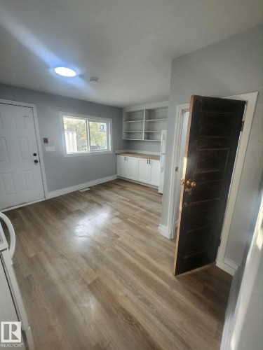 Kitchen area featuring wood-finish flooring, white cabinetry with light countertops, a white exterior door, and a skylight - 11308 94 Street, Edmonton, AB 