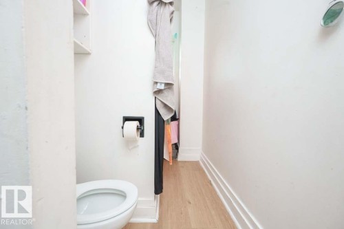 Compact water closet featuring a white toilet, light wood-finish flooring, and white wall shelving - 11308 94 Street, Edmonton, AB 