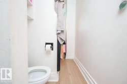 Compact water closet featuring a white toilet, light wood-finish flooring, and white wall shelving - 