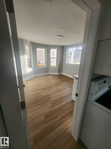 Bright interior space featuring light wood-finish flooring, a bay window with multiple panes, and a flush-mount ceiling light fixture - 11308 94 Street, Edmonton, AB 