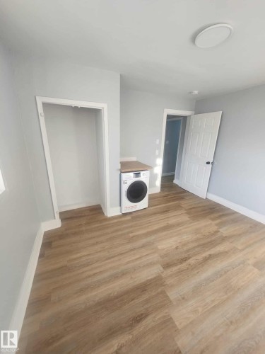 Room featuring wood-finish flooring, light gray walls, a white front-load washer, and a built-in countertop surface - 11308 94 Street, Edmonton, AB 