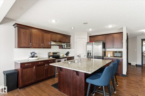 Kitchen featuring wood-finish flooring, dark wood cabinetry, light-toned countertops, a central island with an integrated sink, and stainless steel appliances - 3685 Westcliff Way, Edmonton, AB 
