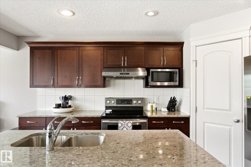 Kitchen featuring granite countertops, dark wood-finish cabinetry, stainless steel appliances, a tile backsplash, and recessed lighting - 3685 Westcliff Way, Edmonton, AB 