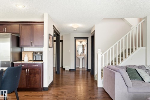Open concept living space featuring rich wood-finish flooring, dark wood cabinetry, stainless steel appliances, a white balustrade staircase, and a pedestal sink in the powder room - 3685 Westcliff Way, Edmonton, AB 