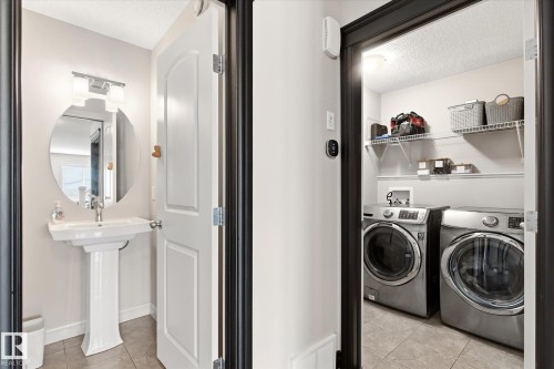 Pedestal sink with an oval mirror and vanity lighting, complemented by an adjacent laundry area featuring wire shelving - 3685 Westcliff Way, Edmonton, AB 