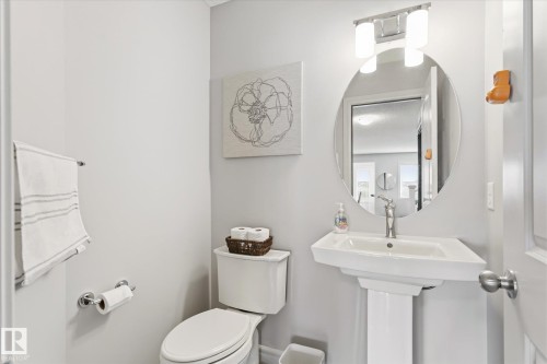 Pedestal sink with chrome faucet, circular mirror, and two-light vanity fixture - 3685 Westcliff Way, Edmonton, AB 