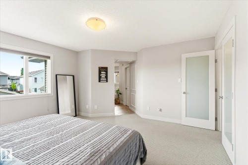 Carpeted room featuring a large window, a frosted glass panel door, and a flush mount ceiling light - 3685 Westcliff Way, Edmonton, AB 
