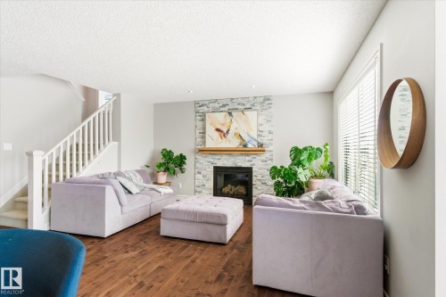 Spacious living area featuring a stone-clad fireplace with a wood mantel, wood-finish flooring, and a white staircase with balusters - 3685 Westcliff Way, Edmonton, AB 