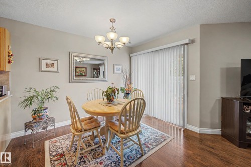 Dining area featuring wood-finish flooring, a contemporary chandelier, and a sliding glass door with vertical blinds - 21 1850 Mill Woods Road E, Edmonton, AB 