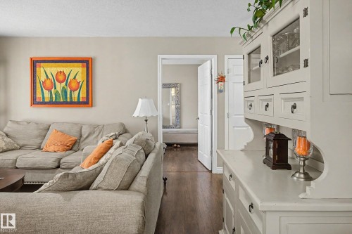 Interior space featuring wood-finish flooring, light neutral wall tones, white trim, and a white built-in hutch with glass-front upper cabinetry - 21 1850 Mill Woods Road E, Edmonton, AB 