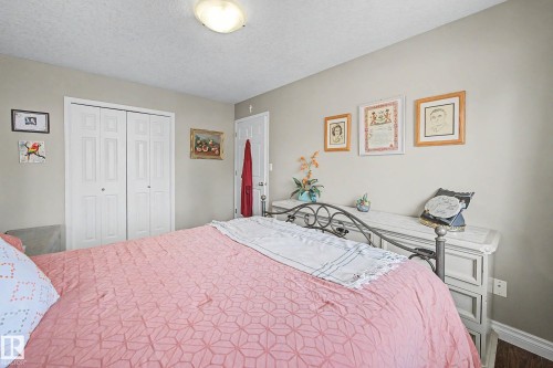 Bedroom featuring light neutral wall tones, white bi-fold closet doors, a white paneled door, wood-finish flooring, and a flush-mount ceiling light fixture - 21 1850 Mill Woods Road E, Edmonton, AB 