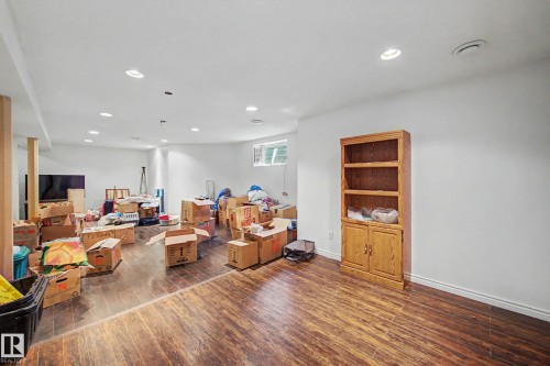 Spacious lower-level room featuring wood-finish flooring, recessed lighting, and white painted walls - 21 1850 Mill Woods Road E, Edmonton, AB 