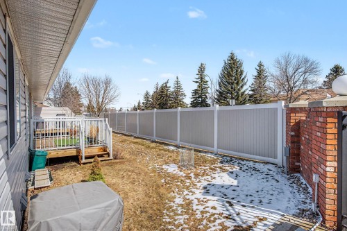 Rear exterior featuring a wood deck with white railings, a partial brick wall, and a full-height privacy fence - 21 1850 Mill Woods Road E, Edmonton, AB 