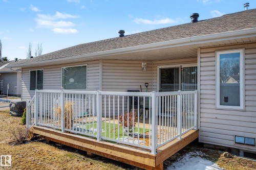 Ground-level deck with white railing, featuring wood-finish decking and direct access to the interior via a sliding glass door - 21 1850 Mill Woods Road E, Edmonton, AB 