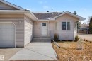Front exterior featuring light-toned horizontal siding, a prominent bay window, and an attached garage with a panel door - 21 1850 Mill Woods Road E, Edmonton, AB 