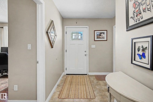 Entryway featuring a white paneled door with decorative glass inserts, neutral wall color, and tile flooring - 21 1850 Mill Woods Road E, Edmonton, AB 