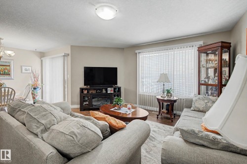 Living area featuring wood-finish flooring and a large window with vertical blinds - 21 1850 Mill Woods Road E, Edmonton, AB 