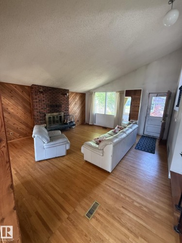 Spacious living area featuring a brick fireplace, wood-finish flooring, and wood paneling - 16321 - 109A Ave, Edmonton, AB - Indoor Photo Showing Living Room With Fireplace
