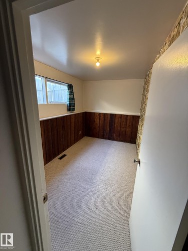 Carpeted room featuring a white ceiling with a single exposed bulb fixture, a window with horizontal panes, and wood-paneled wainscoting - 16321 - 109A Ave, Edmonton, AB - Indoor Photo Showing Other Room