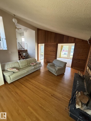 Living area featuring wood-finish flooring, a pitched ceiling, and wood-paneled walls - 16321 - 109A Ave, Edmonton, AB - Indoor Photo Showing Living Room