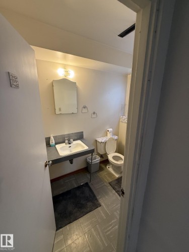 Bathroom featuring a wall-mounted sink with a light-colored basin, a vanity mirror with a decorative frame, and a white toilet - 16321 - 109A Ave, Edmonton, AB - Indoor Photo Showing Bathroom