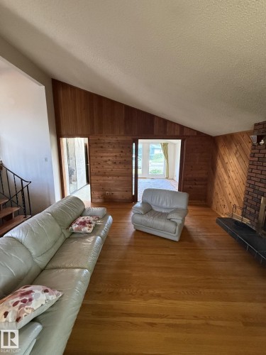 Living area featuring hardwood flooring, wood paneling, a vaulted ceiling, and a brick fireplace with a raised hearth - 16321 - 109A Ave, Edmonton, AB - Indoor