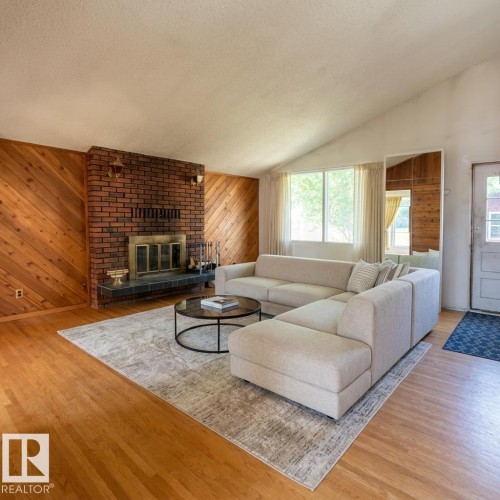 Spacious living area featuring a prominent brick fireplace with a dark stone hearth, wood-finish flooring, and sloped ceilings - 16321 - 109A Ave, Edmonton, AB - Indoor Photo Showing Living Room With Fireplace