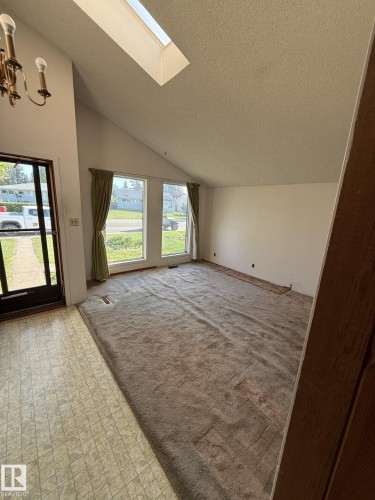 Vaulted ceiling living area featuring a skylight, two large windows, a patterned vinyl entry, and a brass-tone chandelier - 16321 - 109A Ave, Edmonton, AB - Indoor Photo Showing Other Room