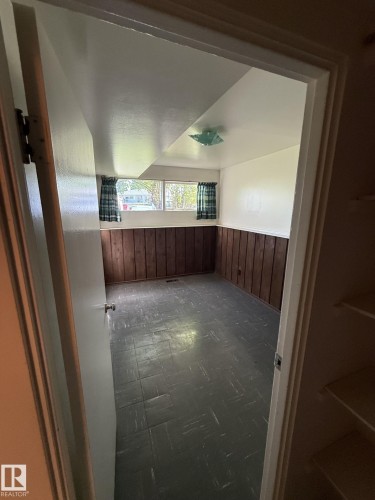Room featuring wood paneling, an overhead light fixture, and a window with a green and white checkered curtain - 16321 - 109A Ave, Edmonton, AB - Indoor