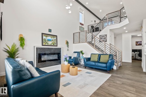 Living area featuring vaulted ceilings, a contemporary fireplace with a black brick surround, and a multi-level staircase with horizontal metal railings - 23 Elwyck Gate, Spruce Grove, AB 