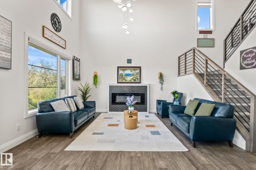 Two-story living area featuring wood-finish flooring, a contemporary fireplace with dark brick surround, and a floating staircase with modern metal balusters - 23 Elwyck Gate, Spruce Grove, AB 