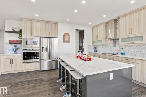 Spacious kitchen featuring a large central island with a white veined countertop, light wood-finish cabinetry, stainless steel appliances, a mosaic tile backsplash, and recessed ceiling lighting - 23 Elwyck Gate, Spruce Grove, AB 