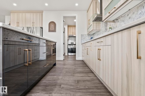 Contemporary kitchen featuring two-tone cabinetry with gold-tone hardware, a light-toned countertop, and a mosaic tile backsplash - 23 Elwyck Gate, Spruce Grove, AB 
