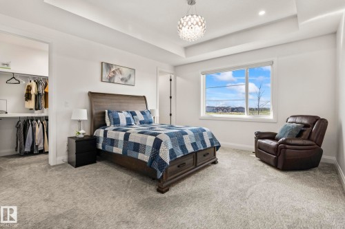 Spacious bedroom featuring light gray carpeting, a large window, and a tray ceiling with a contemporary light fixture - 23 Elwyck Gate, Spruce Grove, AB 