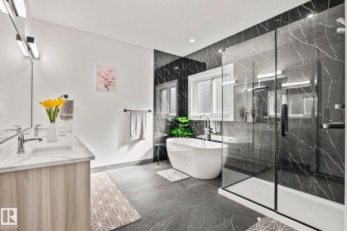 Contemporary bathroom featuring a freestanding soaking tub, a spacious glass-enclosed shower, dual vanity with a marble-finish countertop, dark marble-look wall tiling, and dark tile flooring - 23 Elwyck Gate, Spruce Grove, AB 