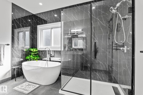 Contemporary bathroom featuring a freestanding soaking tub, a frameless glass shower enclosure, dark patterned wall tiles, recessed lighting, and a white framed window - 23 Elwyck Gate, Spruce Grove, AB 