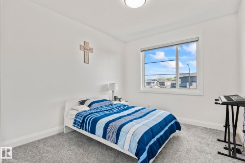 Bright bedroom featuring a large window, plush gray carpeting, white baseboards, and a contemporary ceiling light fixture - 23 Elwyck Gate, Spruce Grove, AB 